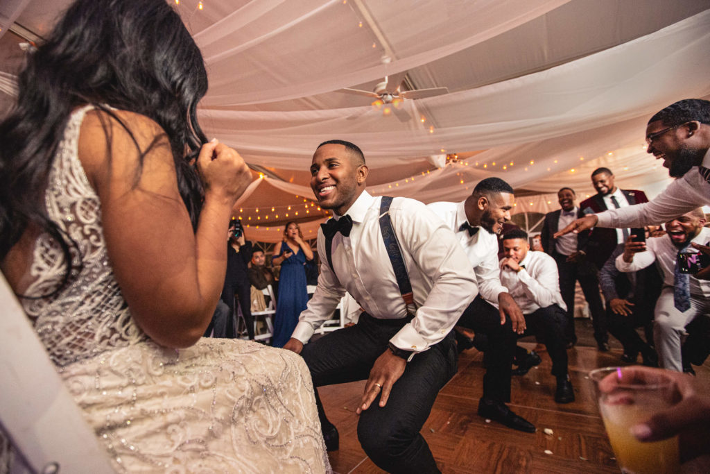 Photojournalistic wedding photography groom dances for bride with fraternity brothers