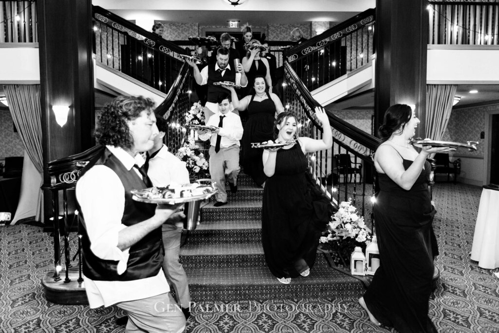 Groomsmen and bridesmaids walking down the staircase carrying the food